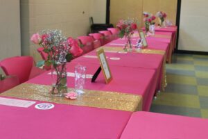 A row of tables decorated with pink covers, flowers and placemats.